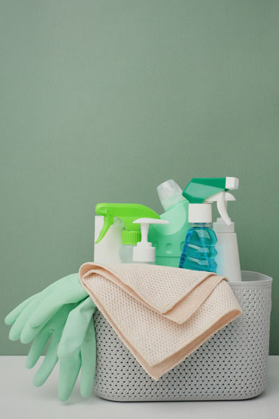 Bottles of detergents rubber gloves and a microfiber cloth are in a light-colored plastic basket